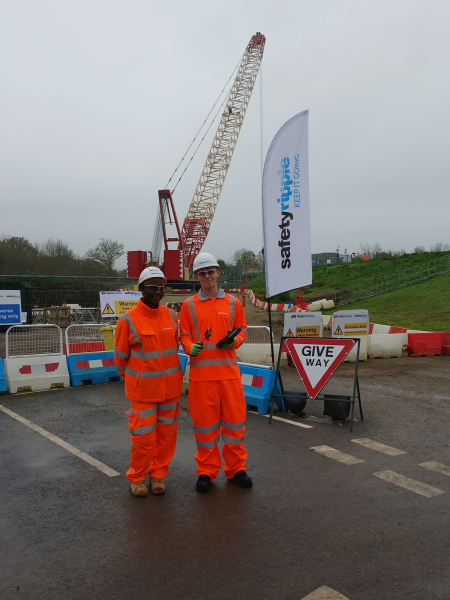 Two men in PPE stood in front of a crane.