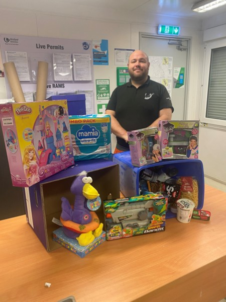 man stood in front of a table with food and toy donations