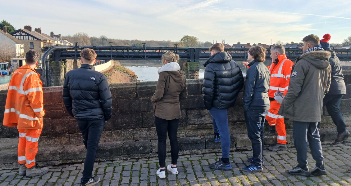 Group of men and women standing on a bridge looking over the bridge wall along the river