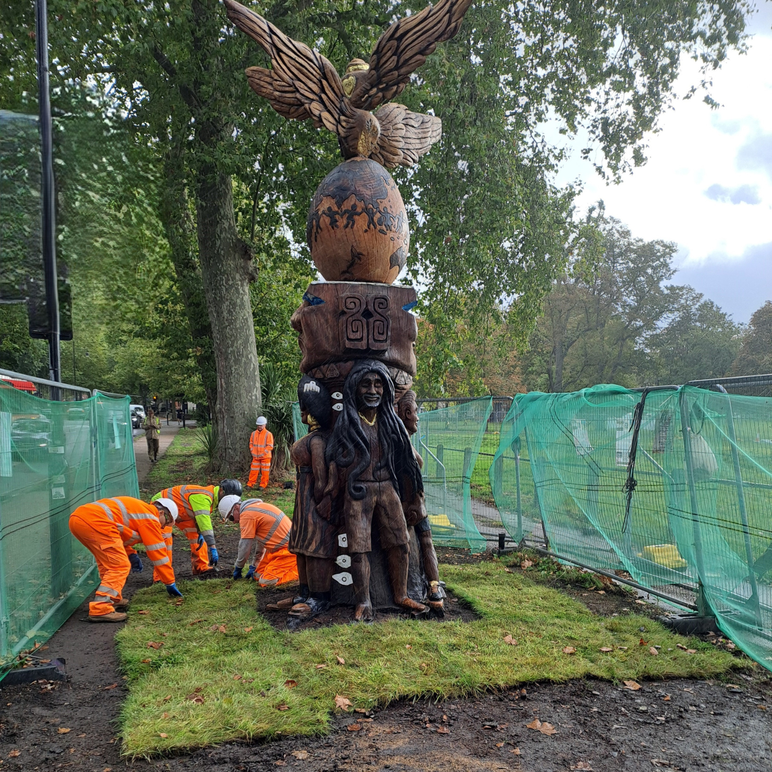 Construction workers laying new turf at the bottom of a totem pole.